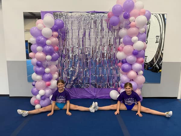 Purple, lavender and pink balloon columns framing a silver sequin backdrop with two cheerleaders posing in splits