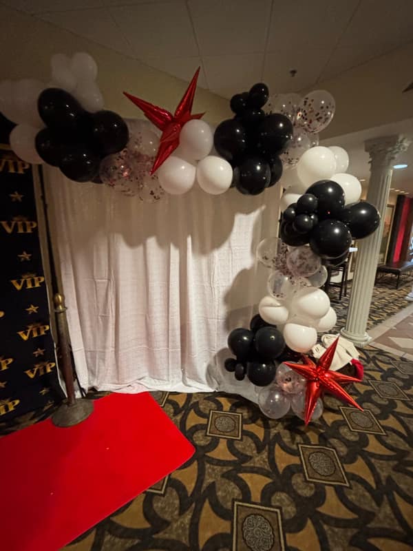 Black, white and confetti balloon arch with red star accents flanking a photo backdrop