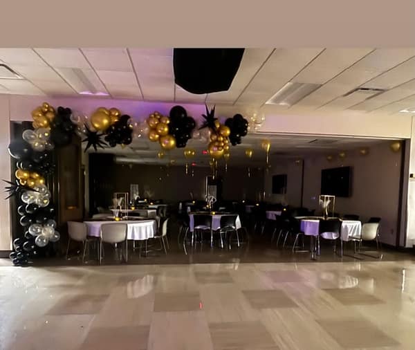 Black, gold and confetti balloon garland with gold starburst accents across a banquet hall entrance