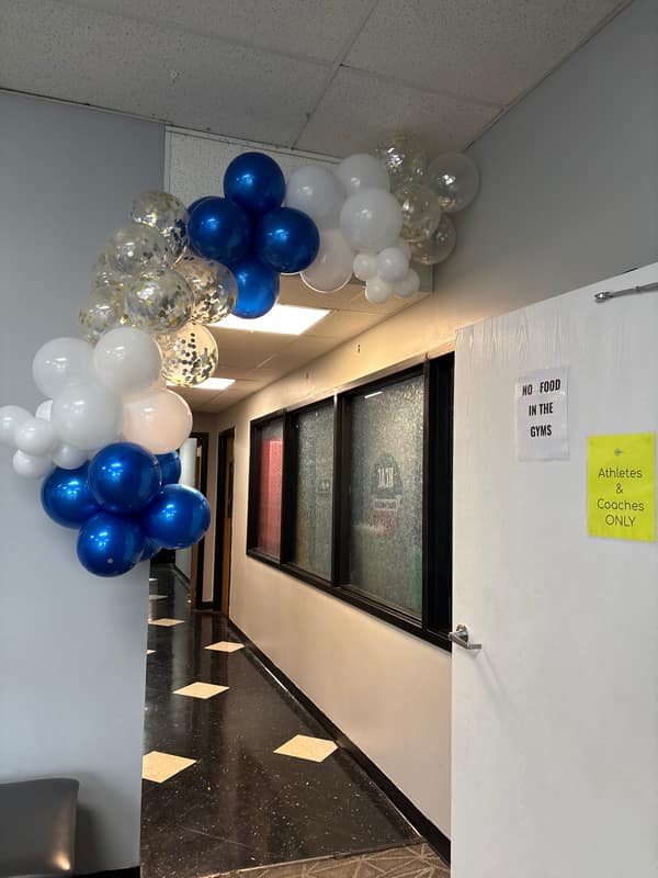Royal blue, white and gold confetti balloon garland arching over a hallway entryway for a school celebration